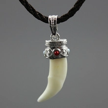 Close-up of ivory-colored wolf tooth pendant with silver metal cap and woven cord