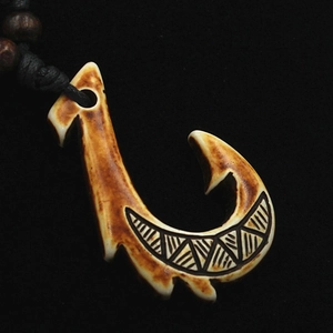 Close-up of Maori fish hook pendant with tribal carvings and brown aged finish