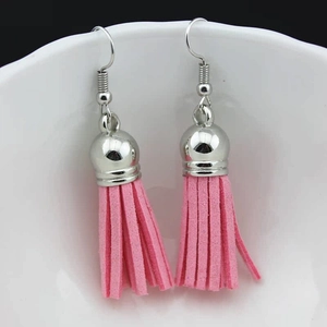 Detail view of pink suede tassel earrings hanging on white ceramic edge with silver hooks