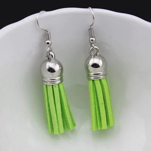 Close-up of vibrant neon green velvet tassel earrings with silver caps on a white porcelain bowl