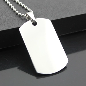 Macro detail of polished stainless steel dog tag pendant with beaded chain on black surface