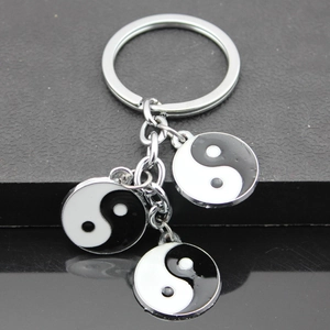 Close-up of silver metal keychain with three Yin Yang pendants on black surface