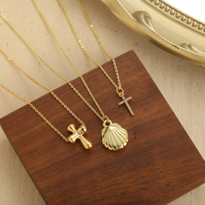 Vintage gold necklaces with shell and cross pendants displayed on wooden blocks