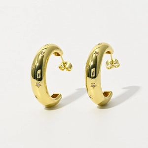 Détail de boucles d'oreilles créoles dorées en C avec petites gravures d'étoiles
