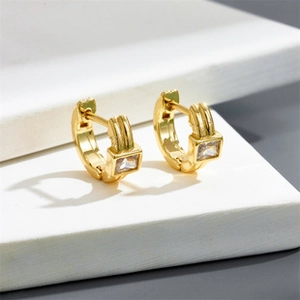 Gros plan de boucles d'oreilles dorées avec zircon carré sur un socle blanc