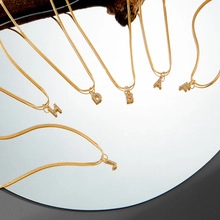 Detailed close-up of multiple minimalist 14K gold plated snake chain necklaces with letter charms
