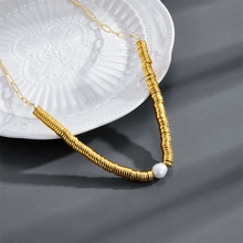 Detail of gold disc bead necklace featuring a white pearl on an embossed white ceramic plate