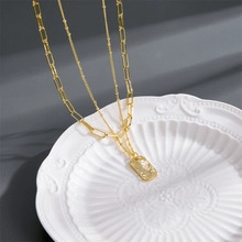 Close-up of gold layered chain necklace with a textured rectangular pendant on white ceramic