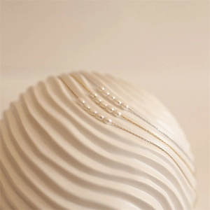 Minimalist freshwater pearl necklaces in gold and silver finish on white wavy pedestal