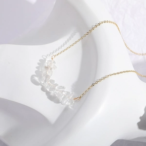 Collar minimalista dorado con colgantes de cristal natural sobre fondo de piedra blanca
