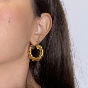 Gros plan de boucles d'oreilles créoles torsadées dorées portées avec une texture élégante