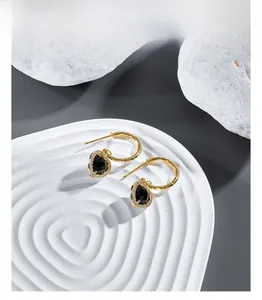Close-up of golden teardrop earrings with faceted black stones and zircon pavé