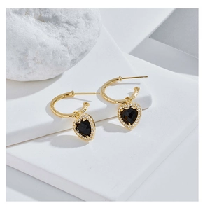 Detailed view of C-shaped gold hoop earrings with black heart pendant and zircon stones