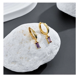 Detail of gold hoop earrings with rectangular purple gemstone pendants on a stone base