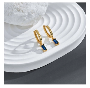 Detailed close-up of gold huggie earrings featuring a rectangle blue zircon stone