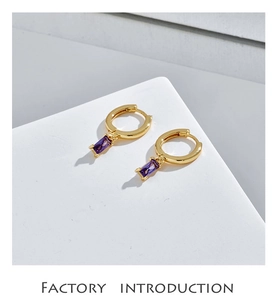 Close-up of golden round hoop earrings featuring rectangular purple zircon stones
