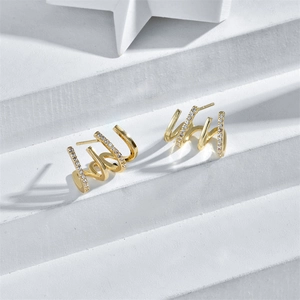 Detail of four-layered gold claw earrings with cubic zirconia inlay on white stairs
