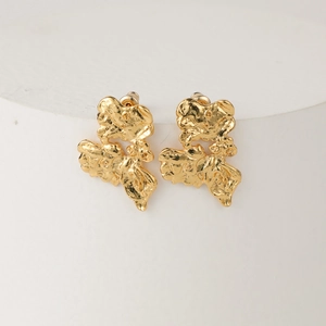 Irregular gold earrings with hammered lava texture on a white display stand