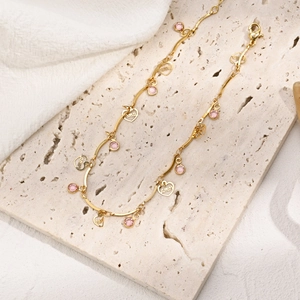 Detail eines 14k vergoldeten Fußkettchens mit rosa Zirkon und Herzanhänger mit Amor-Gravur