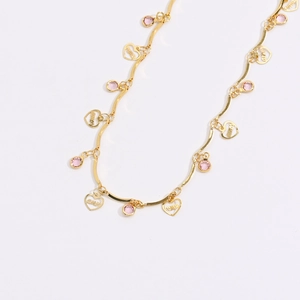 Detailaufnahme einer goldenen Fußkette mit rosa Steinen und Herzanhängern mit Amor-Gravur
