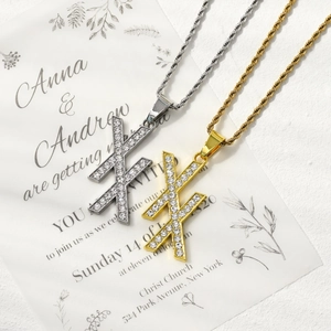 Detail view of gold and silver double X zircon pendants on rope chains over a white card