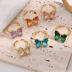 Detailed view of six gold-plated butterfly rings with colorful crystals on a stone plate