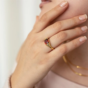 Detailed shot of gold plated brass ring with ruby red oval gemstone and textured band