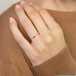 Detailed close-up of a delicate thin gold-plated ring featuring a tiny red crystal butterfly