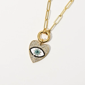 Detailed close-up of gold paperclip chain and heart-shaped evil eye pendant with zircon