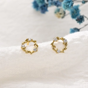 Boucles d'oreilles couronne de feuilles d'olivier dorées avec zircons sur lin blanc pur