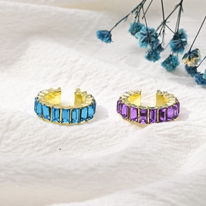 Vintage Ear Cuffs aus Gold mit blauen und lila Zirkonia auf weißem Stoffhintergrund