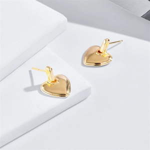 Détail macro de boucles d'oreilles cœur dorées polies sur un support blanc géométrique