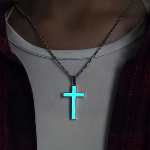 Close-up of glowing blue luminous cross pendant on bead chain worn in dark setting