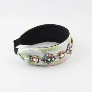 Détail du serre-tête en satin vert avec motifs dorés, strass et perles de luxe