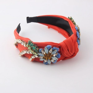 Close-up of orange fabric headband with blue floral embellishments and white rhinestones