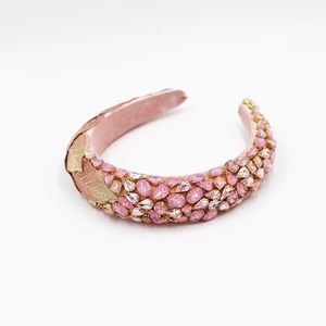 Gros plan d'un serre-tête en velours rose avec strass et détails de feuilles dorées