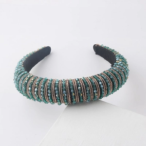 Detail of wide padded headband with green crystals and gold beads on white stone pedestal