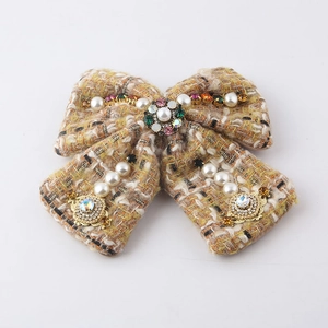 Detailed view of yellow tweed bow accessory with inlaid pearls and colorful crystals