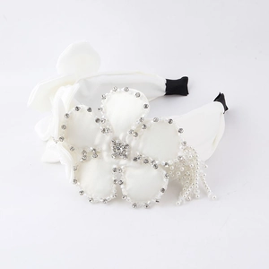 Détail du serre-tête en satin blanc avec fleur en strass et pompons de perles