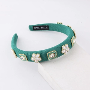 Green fabric padded headband with pearls and crystals on a minimalist white background