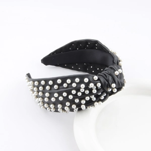 Close-up of a wide black leather headband featuring pearl embellishments and a top knot