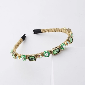 Detailed view of woven gold headband with green crystals and white faux pearls
