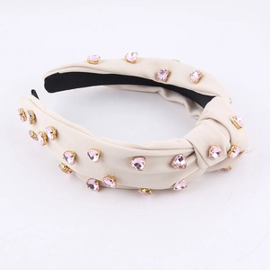 Detalle de diadema con nudo y pedrería de corazón rosa sobre tela sarga crema