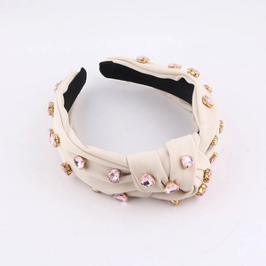 Detalle de diadema beige anudada con cristales de corazón rosa en engastes dorados