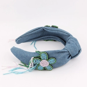 Détail d'un serre-tête en denim bleu avec fleurs perlées à la main et pompons colorés