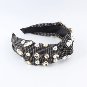 Close-up of wide knotted headband with white pearls and sparkling rhinestones on plaid fabric
