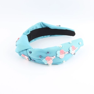 Détail d'un serre-tête bleu clair avec motifs cerises, strass et perles