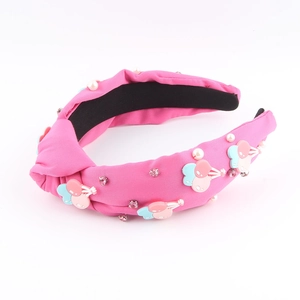 Détail d'un serre-tête rose en tissu noué avec perles et ornements cerise en résine