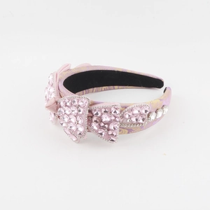 Détail de nœuds en strass roses et motif floral doré sur le serre-tête en satin