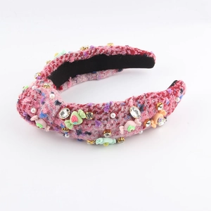 Détail d'un serre-tête en tweed rose avec strass brillants, perles et breloques bonbons